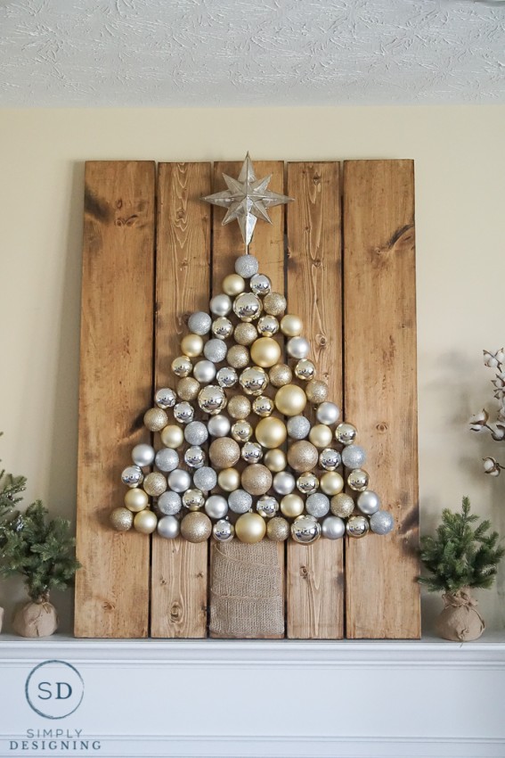 A gold and silver Christmas tree made of Christmas ornaments on a wooden board