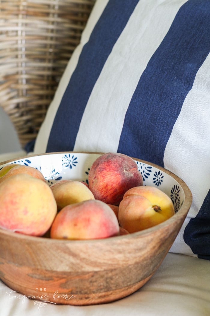 peaches in a bowl with a striped navy and white pillow.