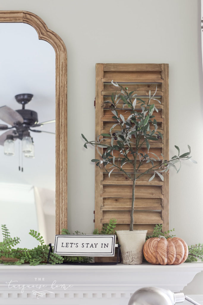 Shutter and olive tree with "let's stay home" sign and a wood grain pumpkin. Fall Mantel Decor