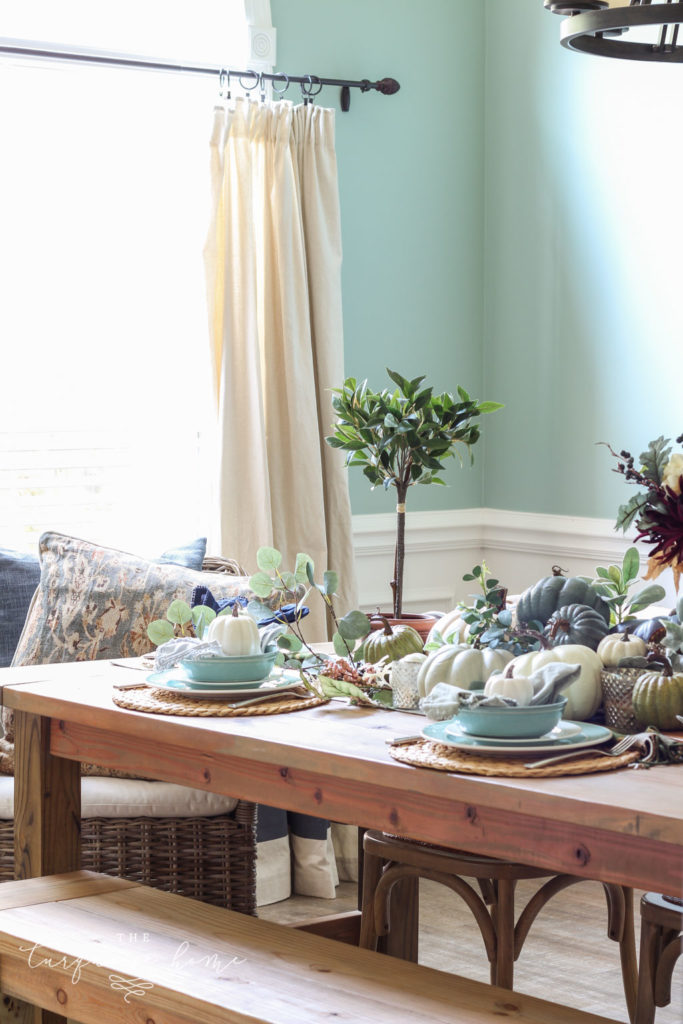 Pumpkins and Greenery Fall Tablescape with bay leaves in a pot and fall floral arrangement. 