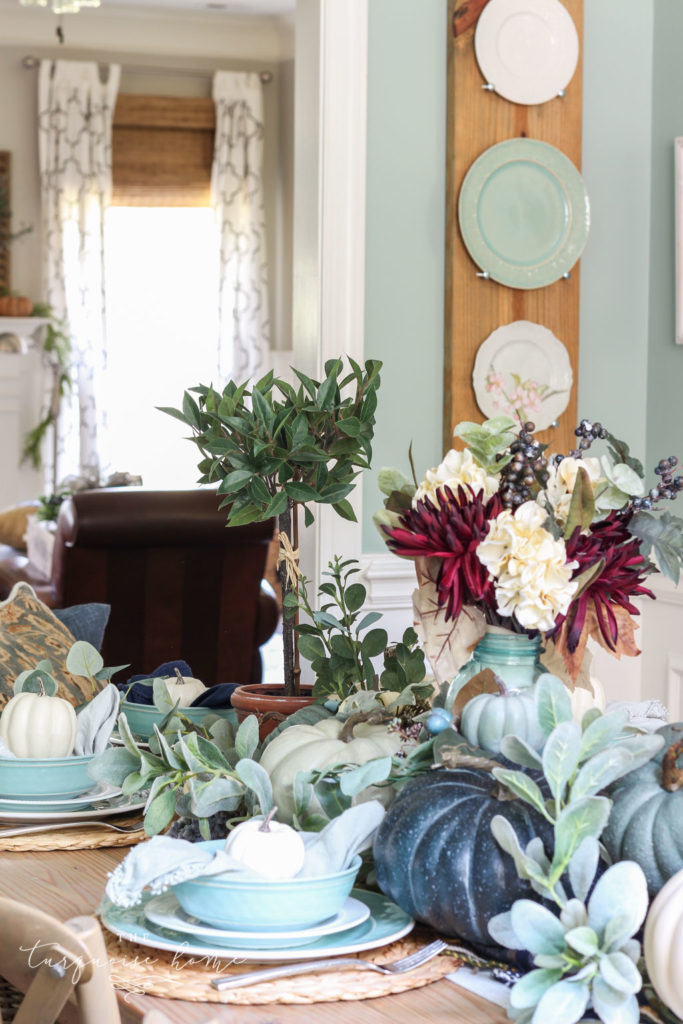 Pumpkins and Greenery Fall Tablescape with bay leaves in a pot and fall floral arrangement. 