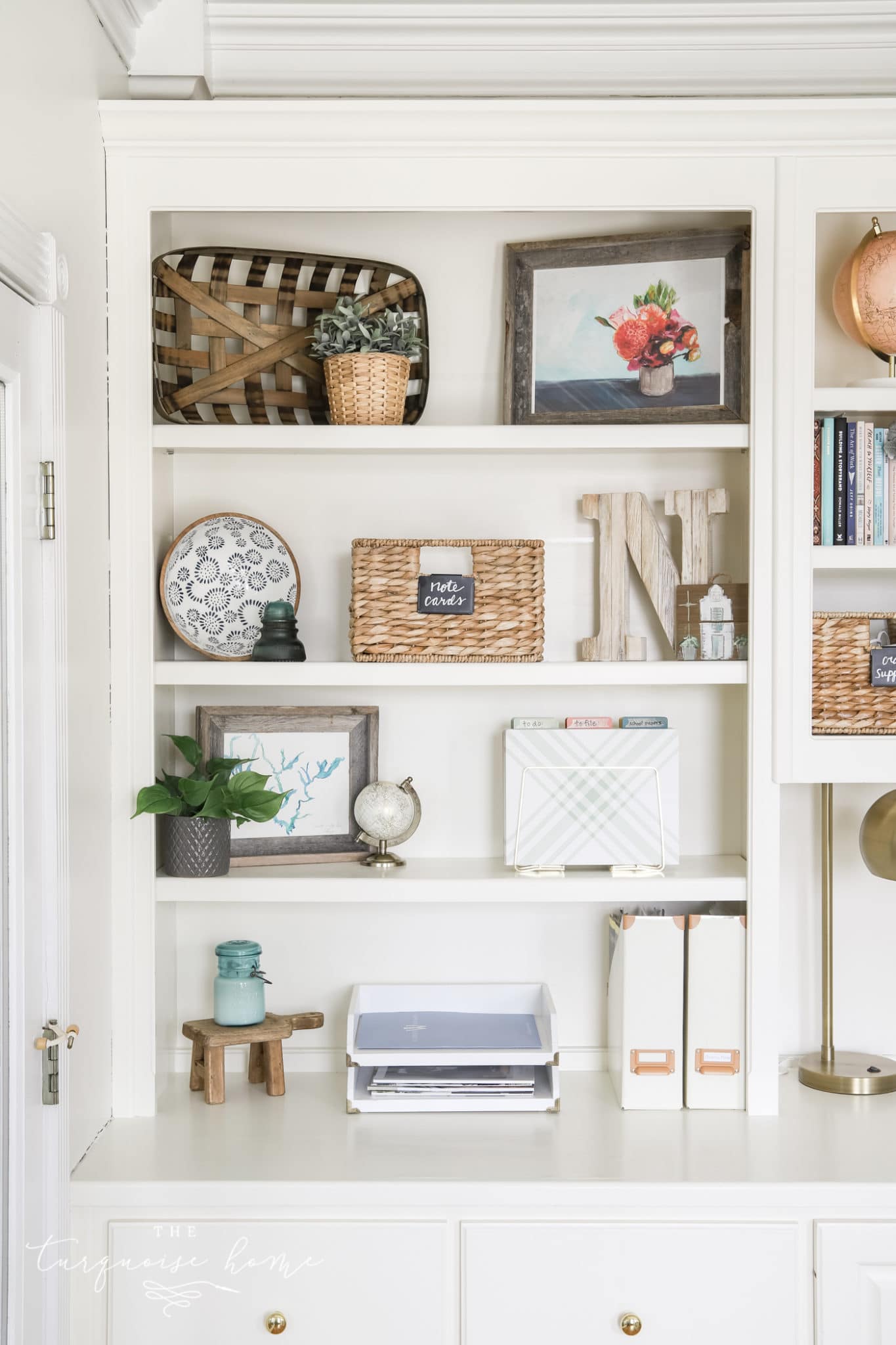 white bookshelves with greenery, books, boxes and art.