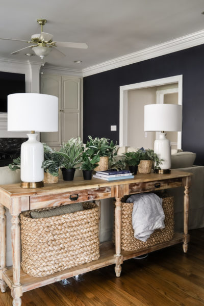 Everett Console Table with console table baskets, white lamps, faux plants and hale navy walls in living room
