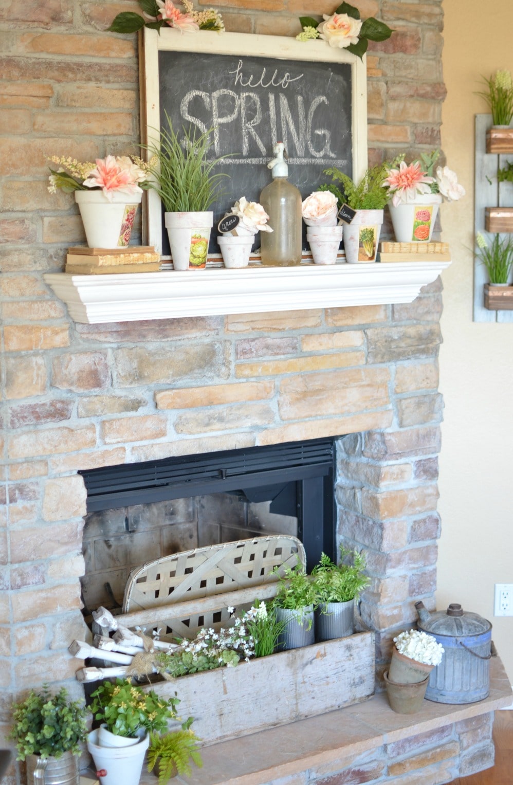 fireplace mantel with spring decor including potted blooms and a sign