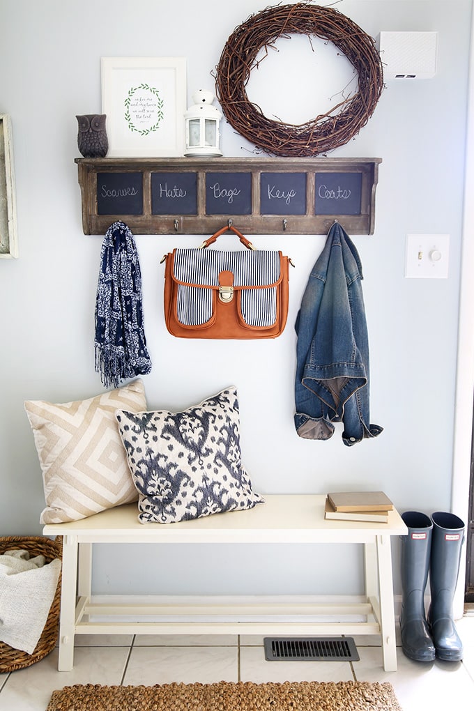 Styled shelf with hooks and chalkboard labels. Bench with throw pillows makes this entryway look cozy.