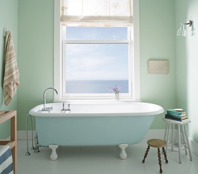 Sunny bathroom with walls painted in Palladian Blue by Benjamin Moore, with a pale blue clawfoot bathtub. 