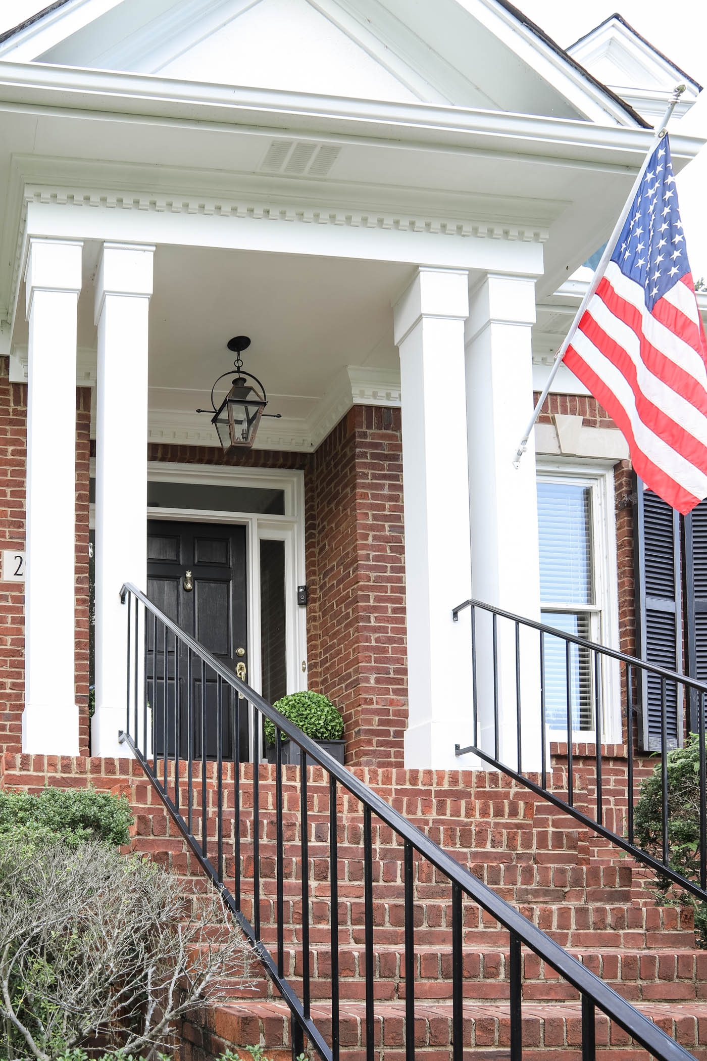 American flag on the front porch of a brick cape cod style home.