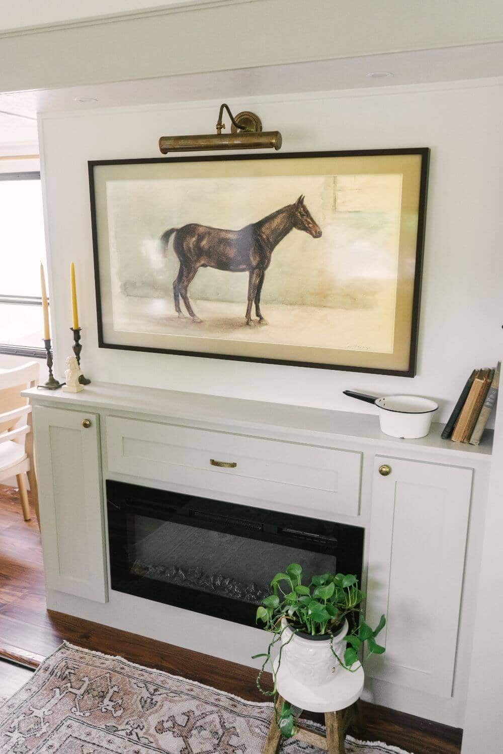 TV above the mantel with a picture light above it and book decor.
