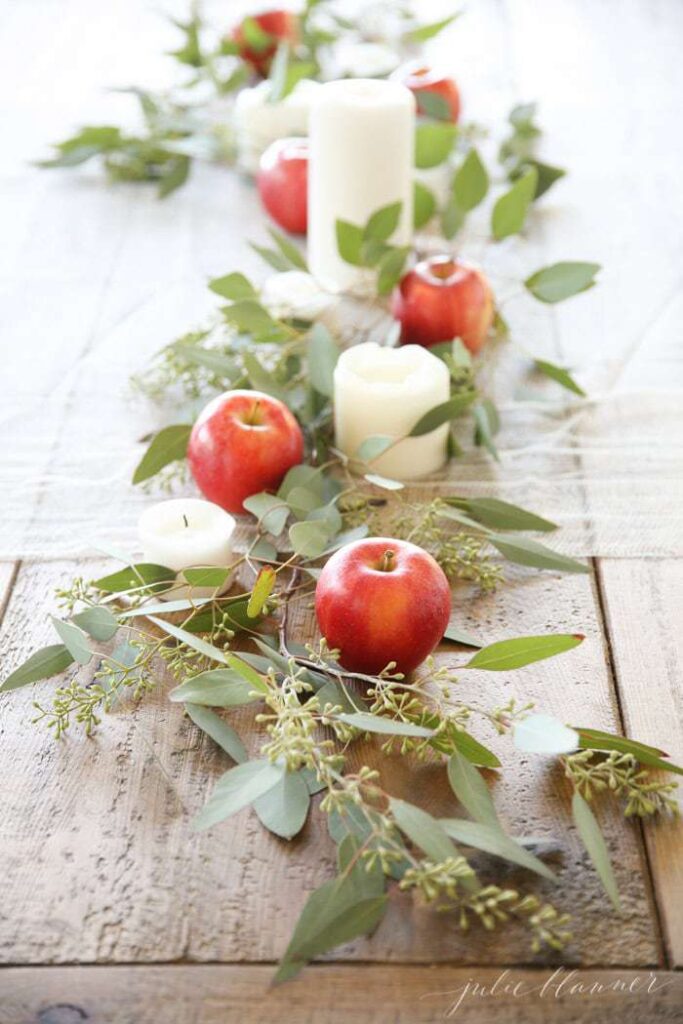 table centerpiece with apple, greenery, and candles.