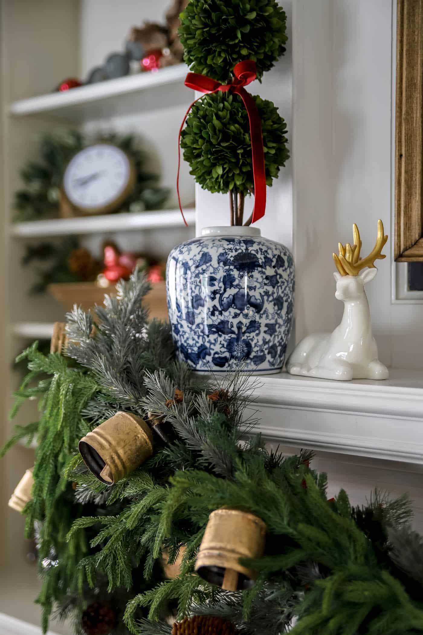 holiday mantel decor with ceramic deer and ginger jar with boxwood topiary and red ribbon