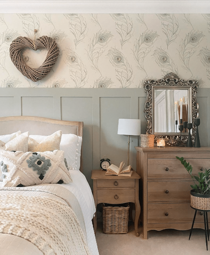 bedroom with Farrow & Ball Mizzle painted board and batten with wallpaper featuring peacock feathers and a heart decor hanging on the wall above the bed.