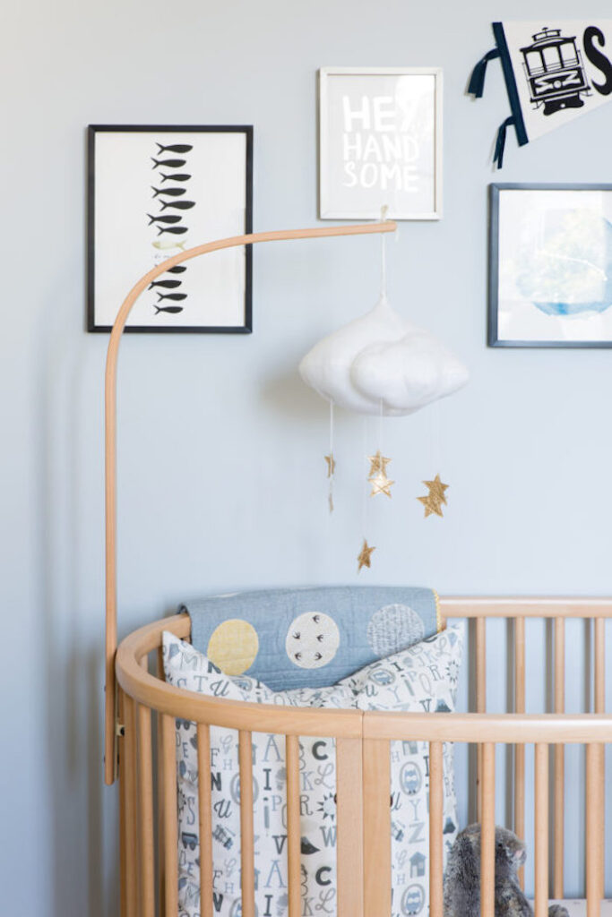 Blue walls in a boy's nursery with cloud hanging mobile and wall art.