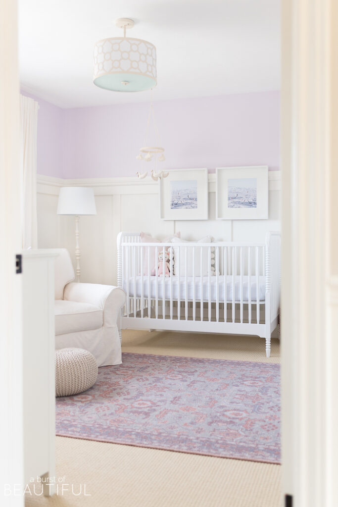 purple wall color in nursery with white crib and white arm chair.