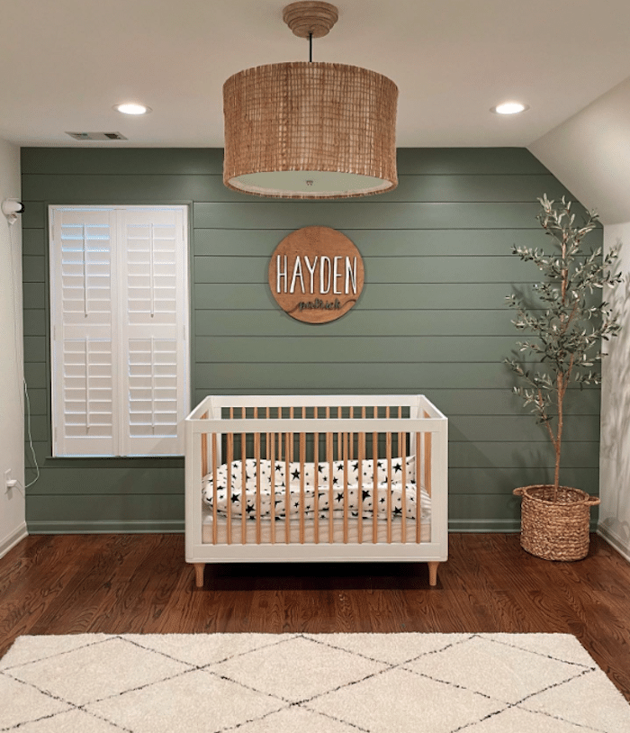 Boy's nursery with green shiplap walls and a modern white and wood crib. 