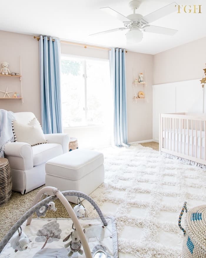 neutral beige nursery with blue curtains and comfortable white rug. 