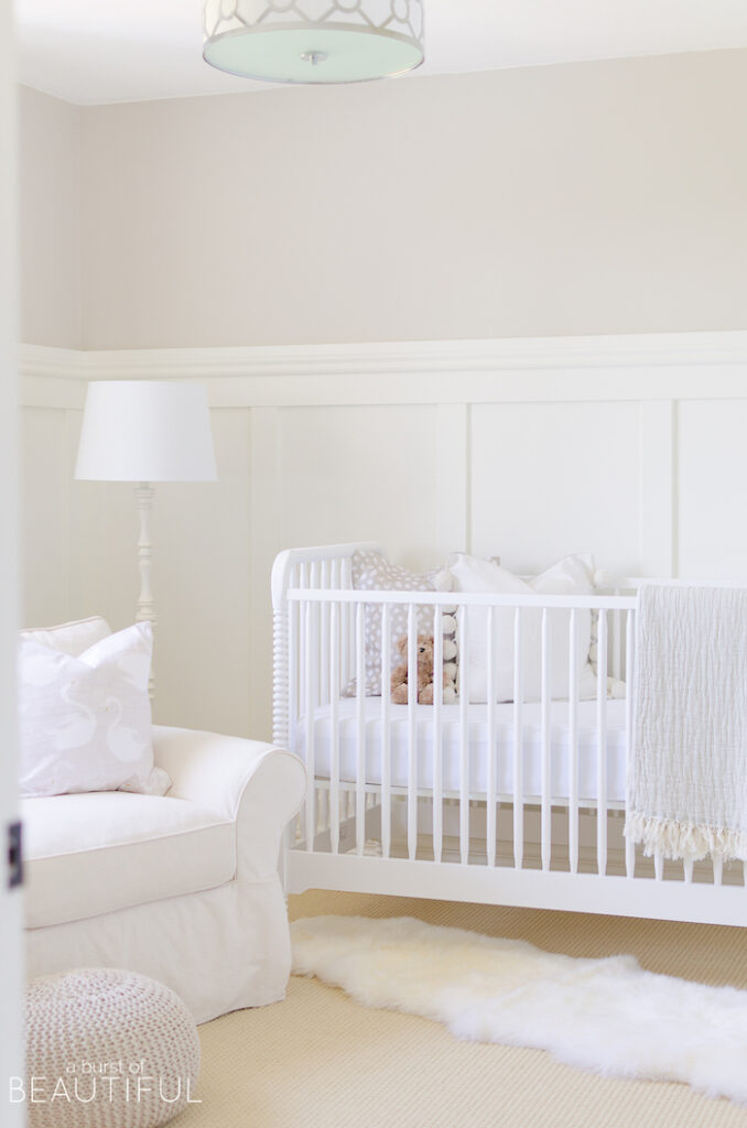 Neutral nursery with Pale Oak walls, white board and batten, white crib, white lamp and white glider rocker. 