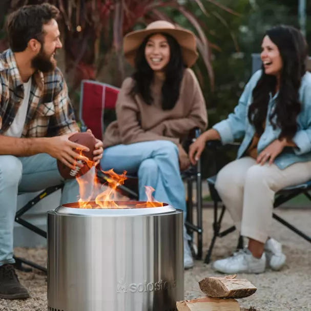 one man and two women sitting in camp chairs around a small Solo Stove fire pit