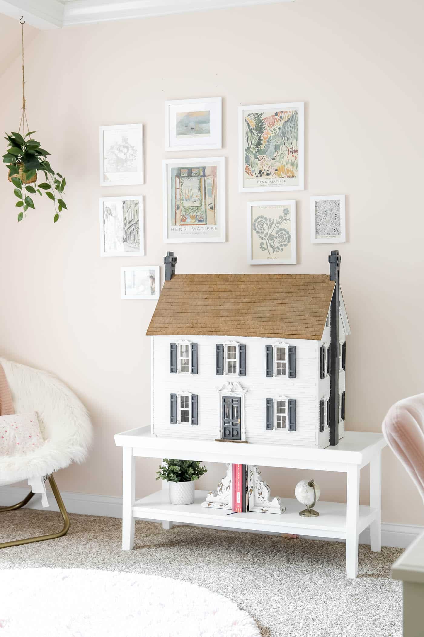 gallery wall on a pink wall with a dollhouse on a coffee table.