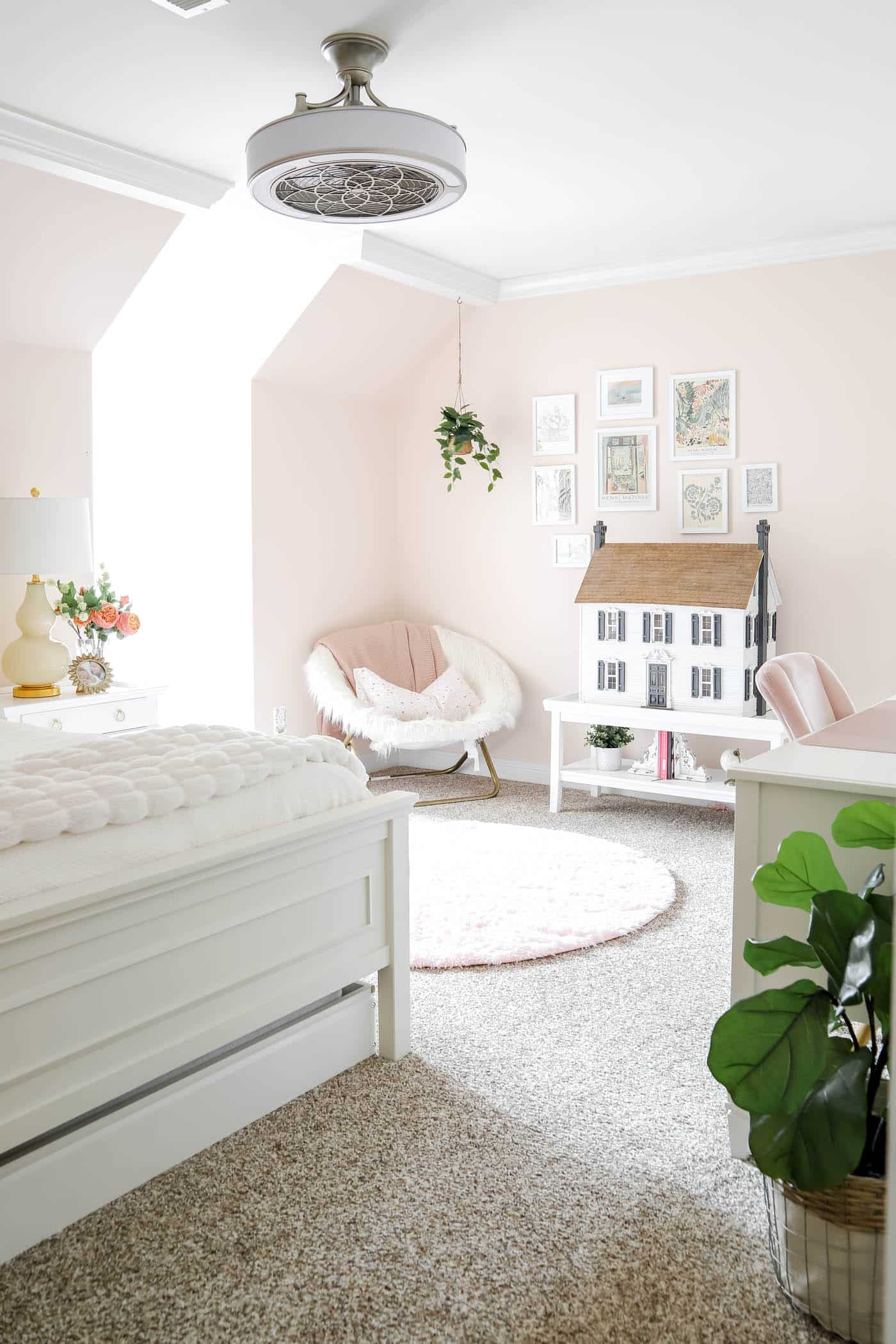 pink teen girl bedroom with doll house on a white coffee table, plush chair in the corner and plant hanging from the ceiling.