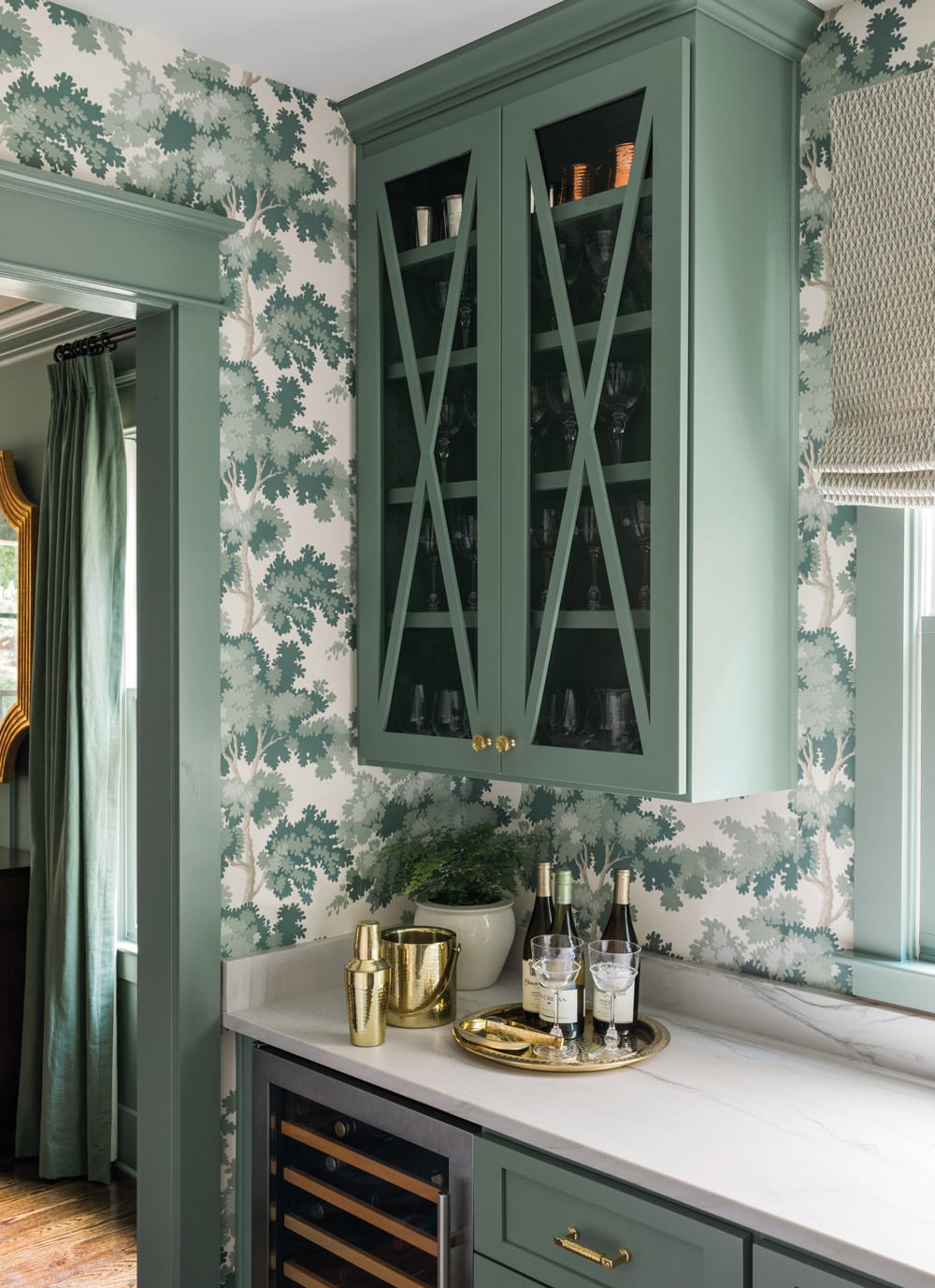 dark green cabinetry and botanicla green wallpaper in a butler's pantry with marble countertops.