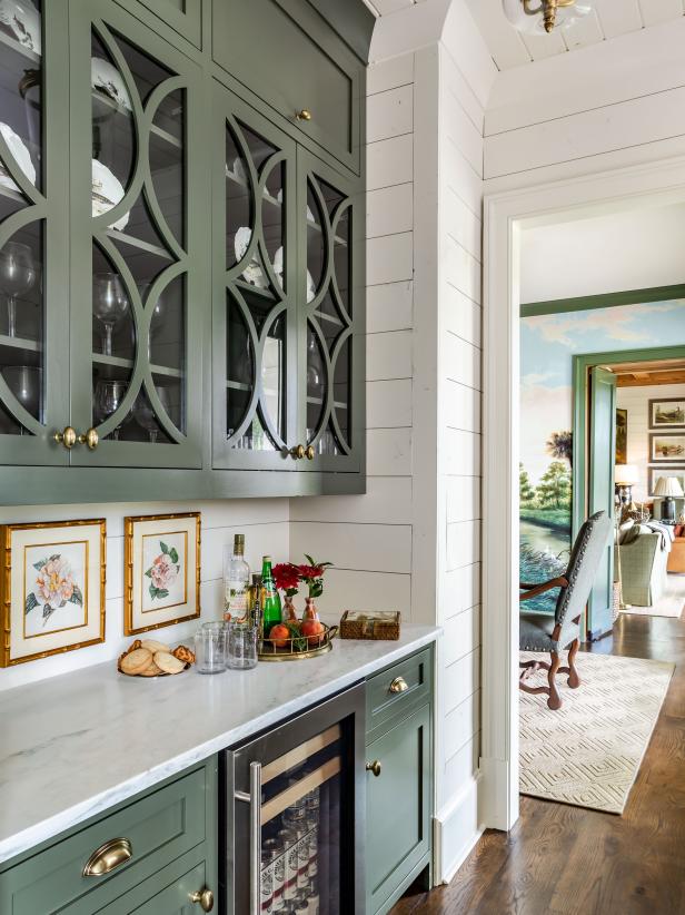 green cabinets in a butler's pantry with white shiplap walls and dark wood floors.