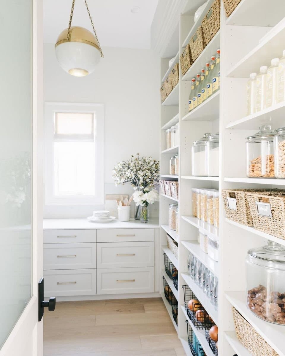 fresh and clean white butler's pantry with light wood floors and window.