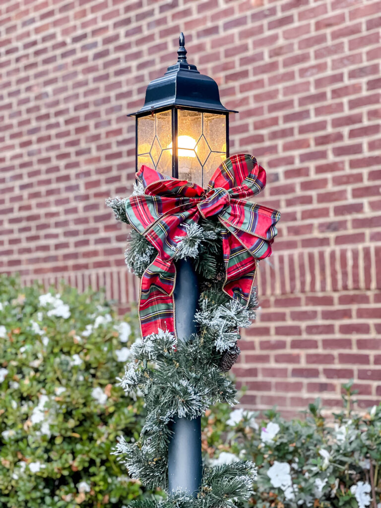 Lamppost with christmas garland and red plaid ribbon on it.