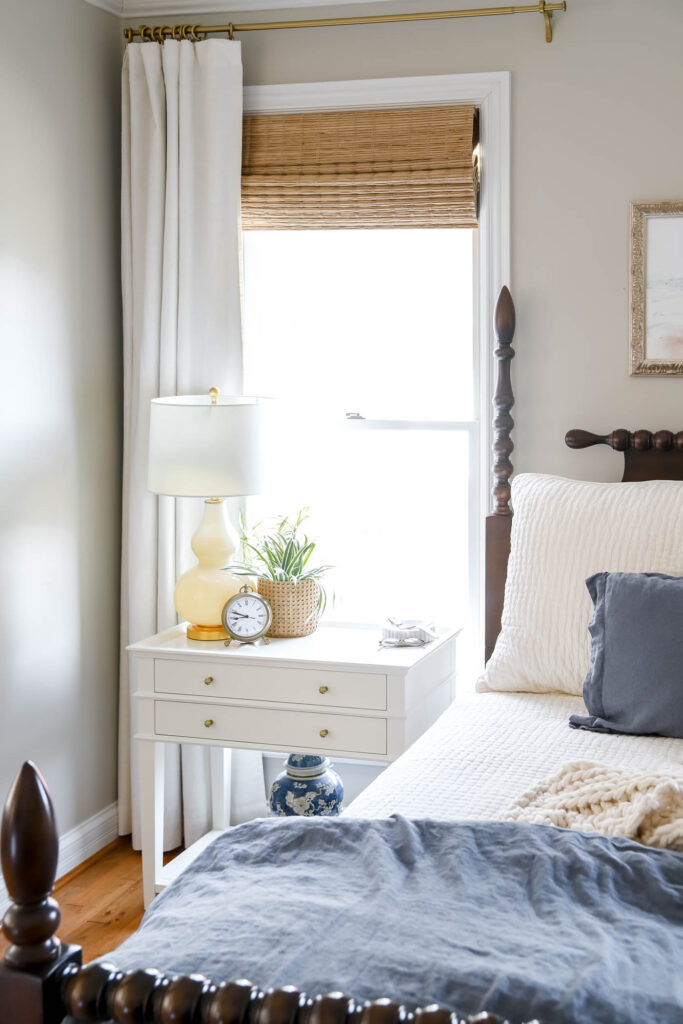 bedroom nightstand with ivory drapes and bamboo roller shades.
