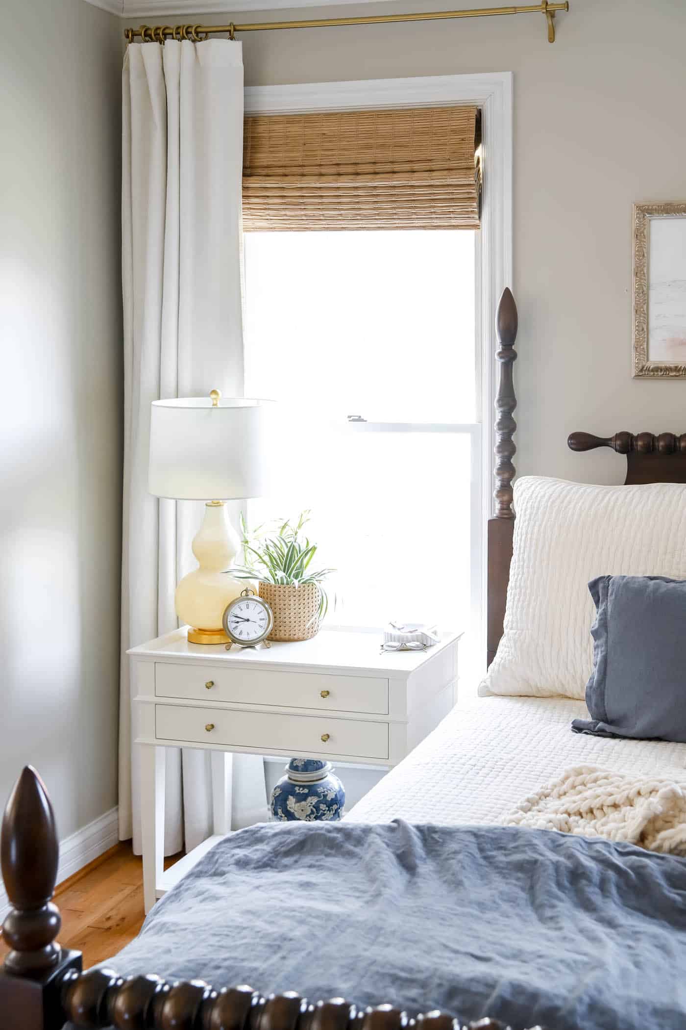 bedroom nightstand with ivory drapes and bamboo roller shades.