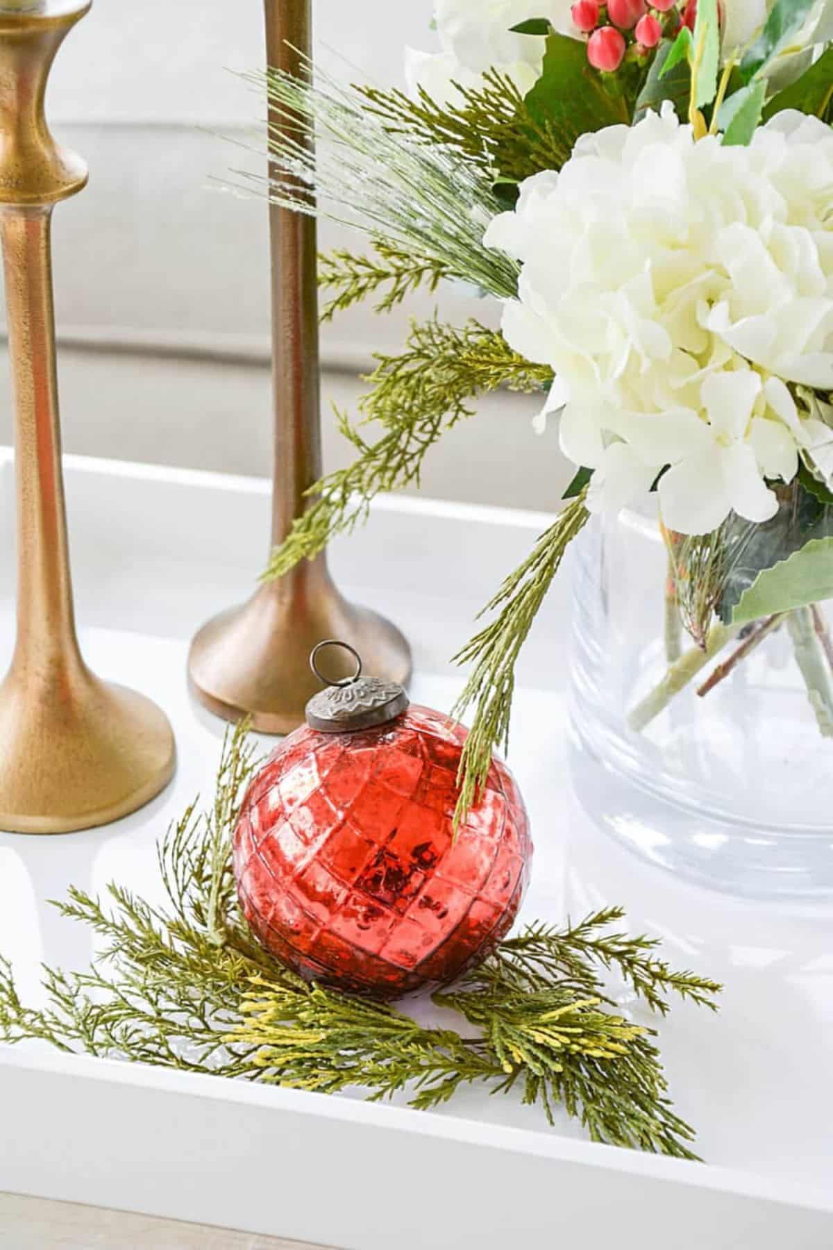 red ornament on some greenery next to flowers and candlesticks.