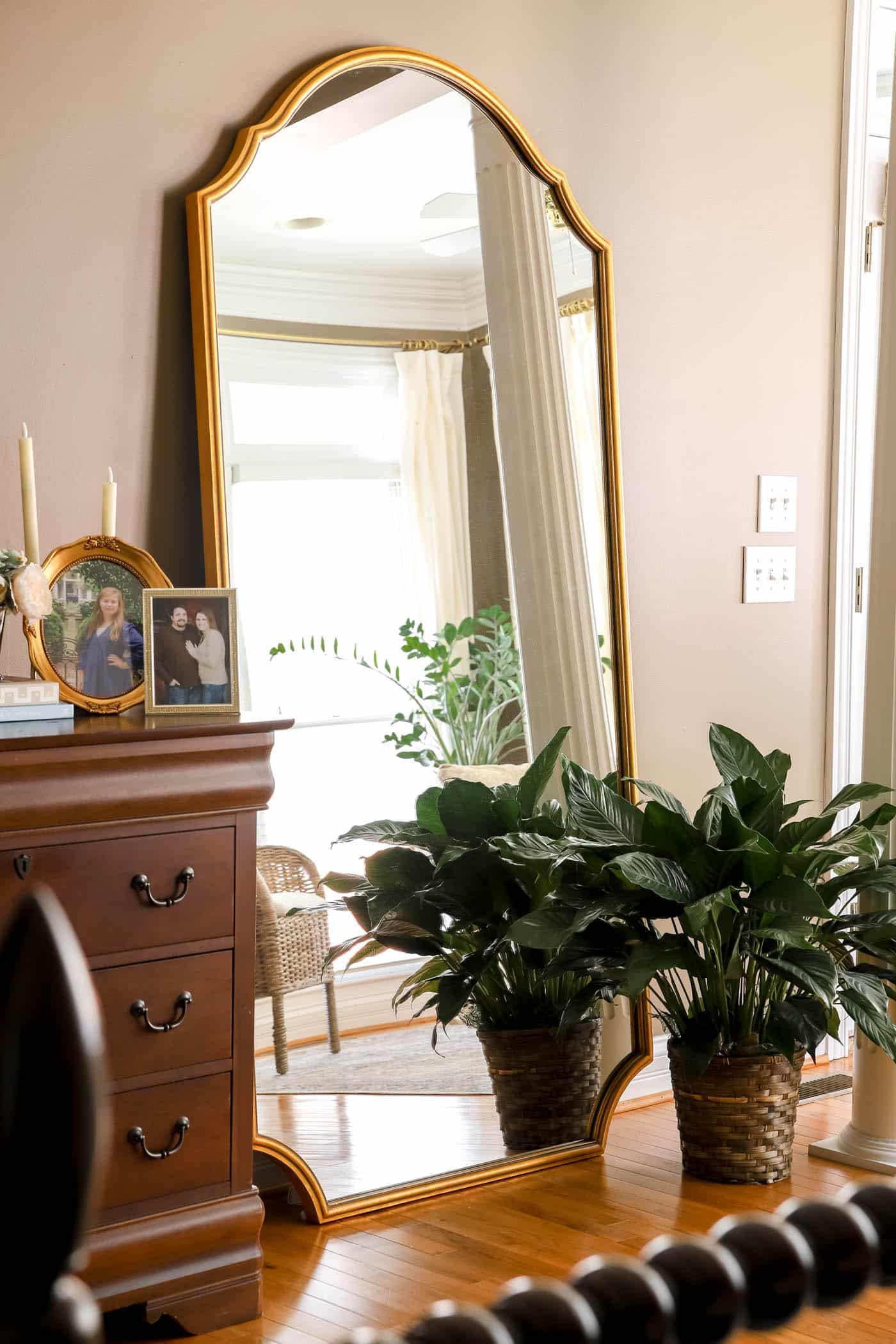 large leaning mirror with a large plant next to it
