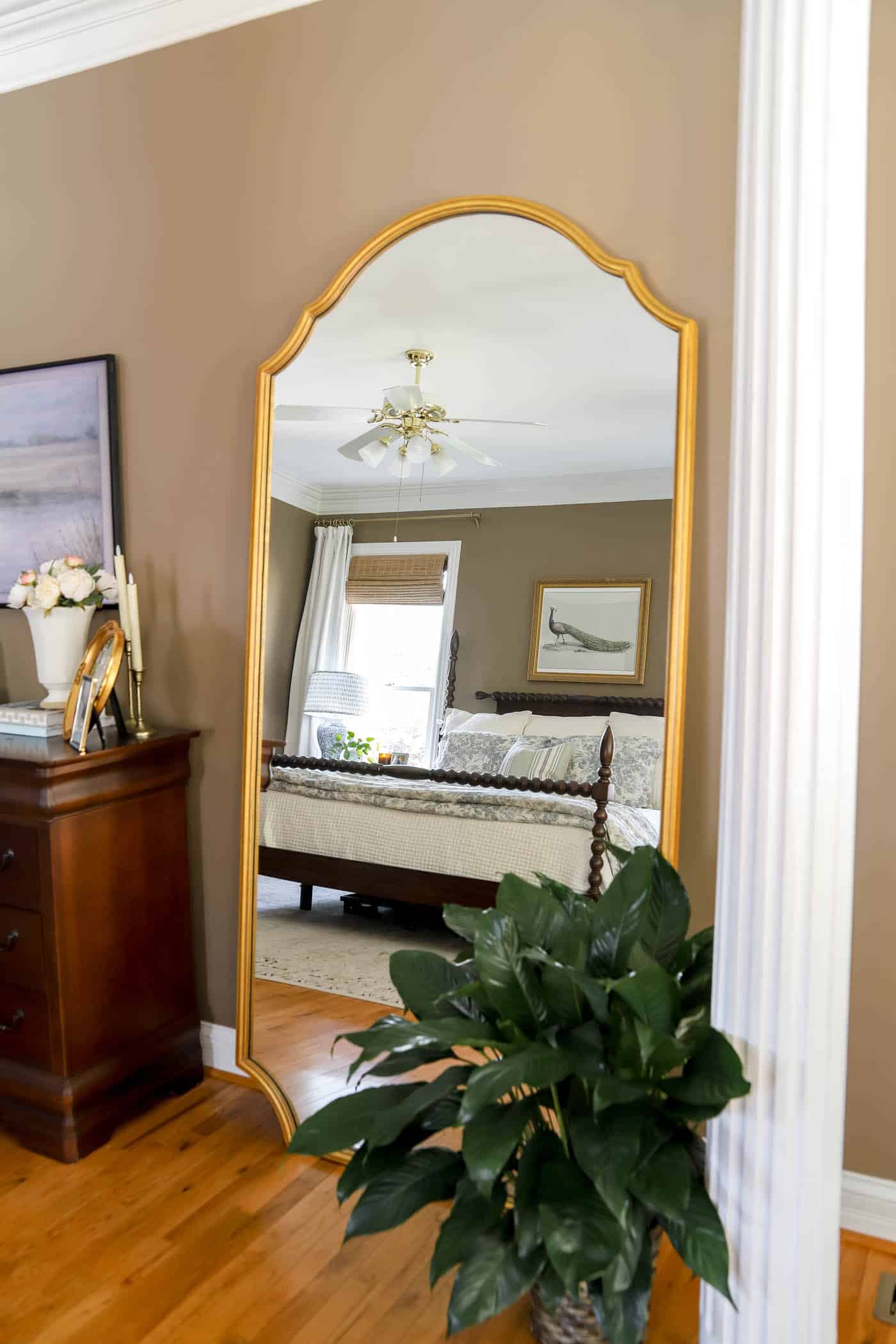 peace lily next to a large mirror with the reflection of a bed.