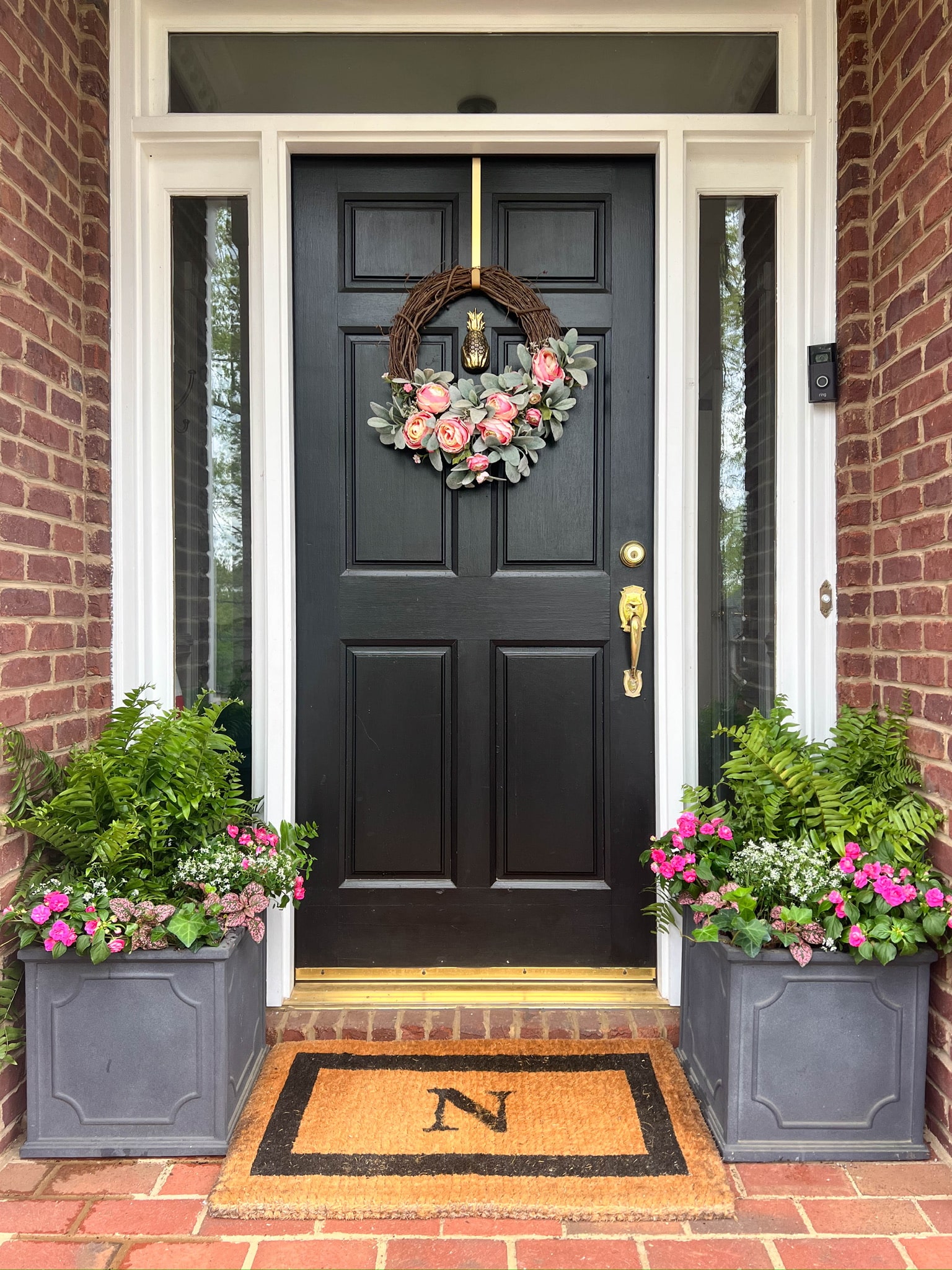 Small front porch ideas with black front door, spring wreath and symmetrical flower planting with pink blooms
