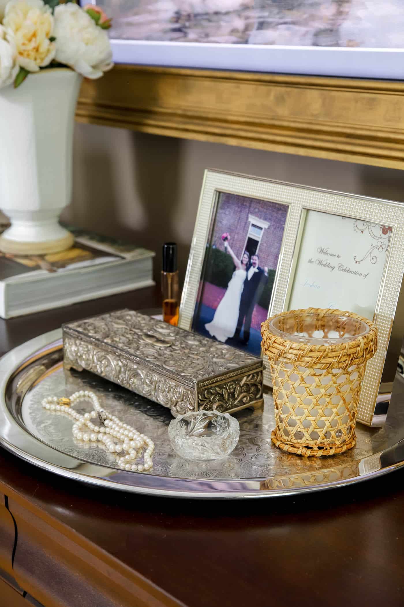 silver tray on a bedroom dresser holding a framed photo, jewelry box and pearl necklaces.